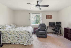 Carpeted bedroom featuring an office area and a ceiling fan