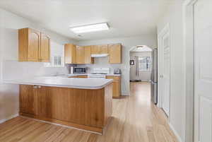 Kitchen featuring light countertops, a peninsula, stainless steel appliances, light wood-style flooring, and healthy amount of natural light