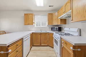 Kitchen with white appliances, light countertops, a peninsula, and light wood finished floors