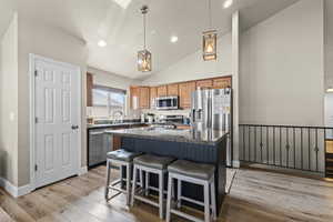 Kitchen with a kitchen island, light wood-style flooring, a kitchen breakfast bar, hanging light fixtures, and stainless steel appliances