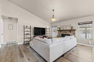 Living room featuring vaulted ceiling, light wood-style flooring, a stone fireplace, and healthy amount of natural light