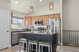 Kitchen with stainless steel appliances, a kitchen island, dark stone countertops, light wood-style flooring, and vaulted ceiling