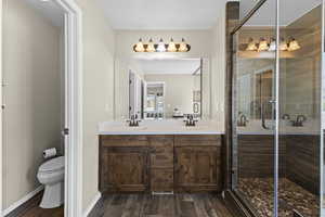 Bathroom with double vanity, wood finish floors, and a stall shower