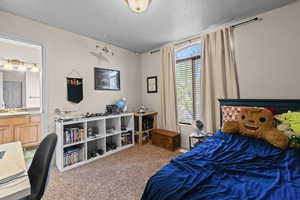 Bedroom with a textured ceiling, light colored carpet, and connected bathroom