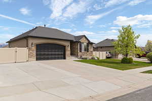View of front of house with a gate, an attached garage, driveway, stone siding, and stucco siding
