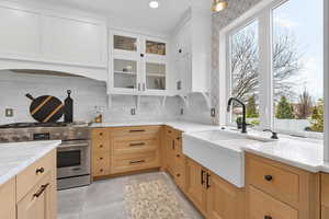 Kitchen with high end range, healthy amount of natural light, light stone counters, glass fronted cabinets, and two tone cabinetry
