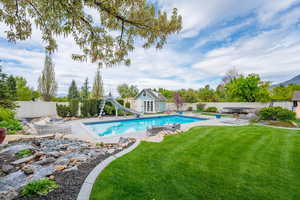 View of pool with an outbuilding, a storage structure, a fenced backyard, a water slide, and patio surround