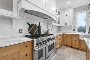 Kitchen with glass fronted cabinets, range with two ovens, tasteful backsplash, light stone countertops, and dual tone cabinetry