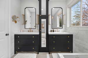 Full bath with tile walls, two vanities, a wainscoted wall, and light tile patterned floors