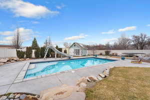 View of pool featuring a fenced backyard, an outbuilding, a storage structure, a water slide, and patio surround
