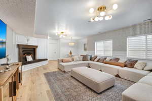 Living area with suspended lighting, wainscoting, a textured ceiling, light wood finished floors, and wallpapered walls