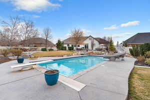View of swimming pool featuring a diving board, a water slide, a fenced backyard, and patio surround