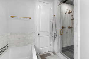 Bathroom with a marble finish shower, a garden tub, and dark tile patterned floors