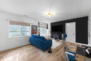 Living area with light wood-type flooring, a textured ceiling, and a desk