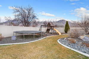 Fenced backyard with a playground, a trampoline, and a mountain view