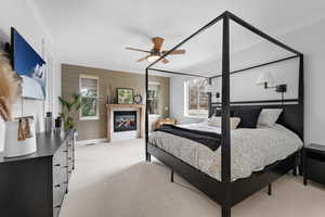 Bedroom with light carpet, a glass covered fireplace, multiple windows, crown molding, and ceiling fan