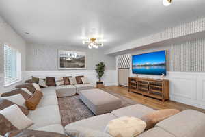 Living room featuring wallpapered walls, wainscoting, wood finished floors, hanging lights, and a decorative wall