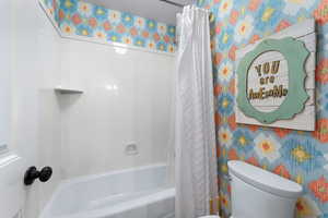 Bathroom with shower / bathtub combination with curtain, wallpapered walls, and a textured ceiling