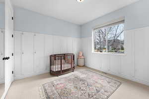 Bedroom with a decorative wall, wainscoting, a crib, and light carpet