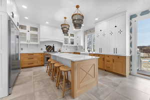 Kitchen featuring two tone cabinets, a kitchen island, light stone counters, decorative backsplash, and glass insert cabinets