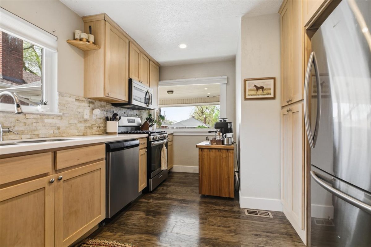 Kitchen featuring light wood finish cabinetry, stainless steel appliances, light countertops, dark wood-style floors, and recessed lighting
