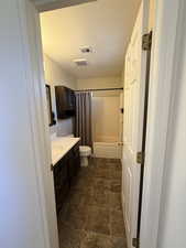 Full bathroom with vanity, a textured ceiling, shower / bath combination with curtain, and dark stone finish flooring
