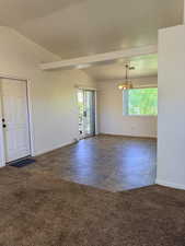 Spare room featuring dark carpet, a chandelier, and lofted ceiling