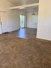 Unfurnished room featuring dark carpet, vaulted ceiling, and hanging lights