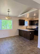Kitchen featuring dark wood finish cabinets, black range with gas stovetop, a peninsula, suspended lighting, and light stone countertops