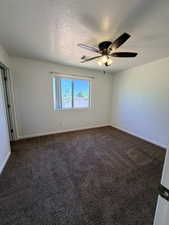 Spare room featuring dark carpet, ceiling fan, and a textured ceiling