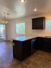 Kitchen featuring dark wood finish cabinets, a peninsula, light stone countertops, a textured ceiling, and suspended lighting