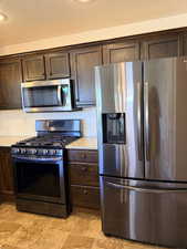 Kitchen with stainless steel appliances, dark wood finish cabinets, a textured ceiling, and light stone countertops