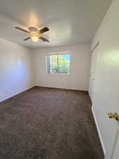 Unfurnished bedroom featuring a textured ceiling, dark carpet, ceiling fan, and a closet
