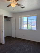 Unfurnished bedroom featuring a closet, a textured ceiling, ceiling fan, and dark colored carpet