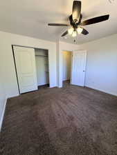 Unfurnished bedroom featuring dark carpet, a textured ceiling, a closet, and a ceiling fan