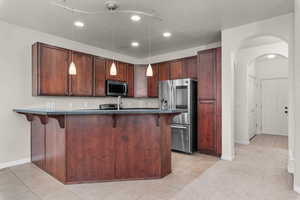 Kitchen with a breakfast bar, light tile patterned flooring, arched walkways, and stainless steel appliances