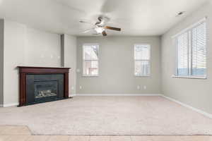 Unfurnished living room with ceiling fan, a tile fireplace, carpet, and tile patterned flooring