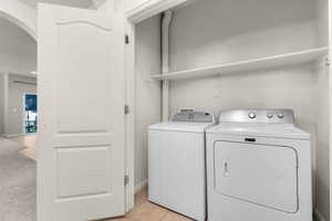 Laundry area with light tile patterned floors, arched walkways, light colored carpet, and washer and clothes dryer