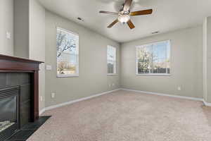 Unfurnished living room with carpet flooring, ceiling fan, plenty of natural light, and a tile fireplace