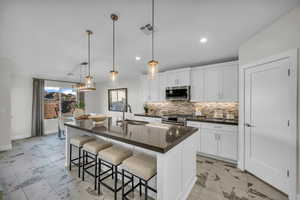 Kitchen with a kitchen bar, white cabinets, and light marble finish flooring