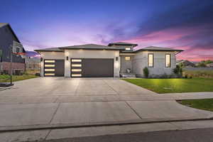 Prairie-style house featuring stone siding, a front yard, concrete driveway, a garage, and stucco siding