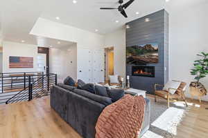 Living area with light wood-style floors, a large fireplace, ceiling fan, and recessed lighting
