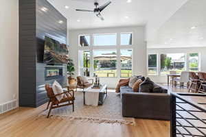 Living room with a ceiling fan, a fireplace, recessed lighting, light wood-type flooring, and a high ceiling