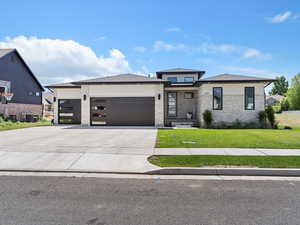 Prairie-style home with stone siding, a garage, a front lawn, concrete driveway, and stucco siding