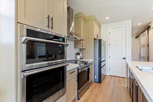 Two tone kitchen featuring stainless steel appliances, light wood-style flooring, backsplash, light stone counters, and recessed lighting