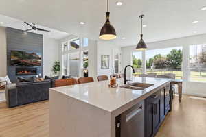 Kitchen featuring open floor plan, light stone counters, hanging light fixtures, a center island with sink, and light wood-type flooring