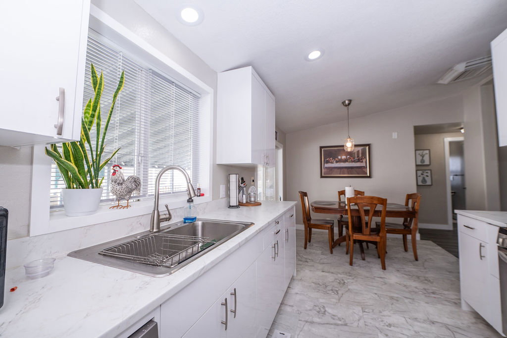Kitchen featuring white cabinets, vaulted ceiling, hanging light fixtures, and light marble finish flooring