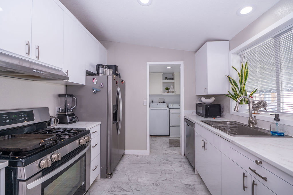 Kitchen featuring stainless steel appliances, white cabinetry, light marble finish flooring, recessed lighting, and independent washer and dryer