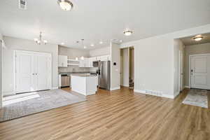 Kitchen featuring white cabinetry, open floor plan, stainless steel appliances, a kitchen island, and light wood-type flooring