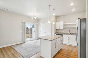 Kitchen featuring freestanding refrigerator, a center island, white cabinetry, light stone countertops, and light wood-type flooring